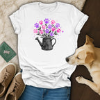 White t-shirt with black watering can overflowing with pink and purple paw prints.