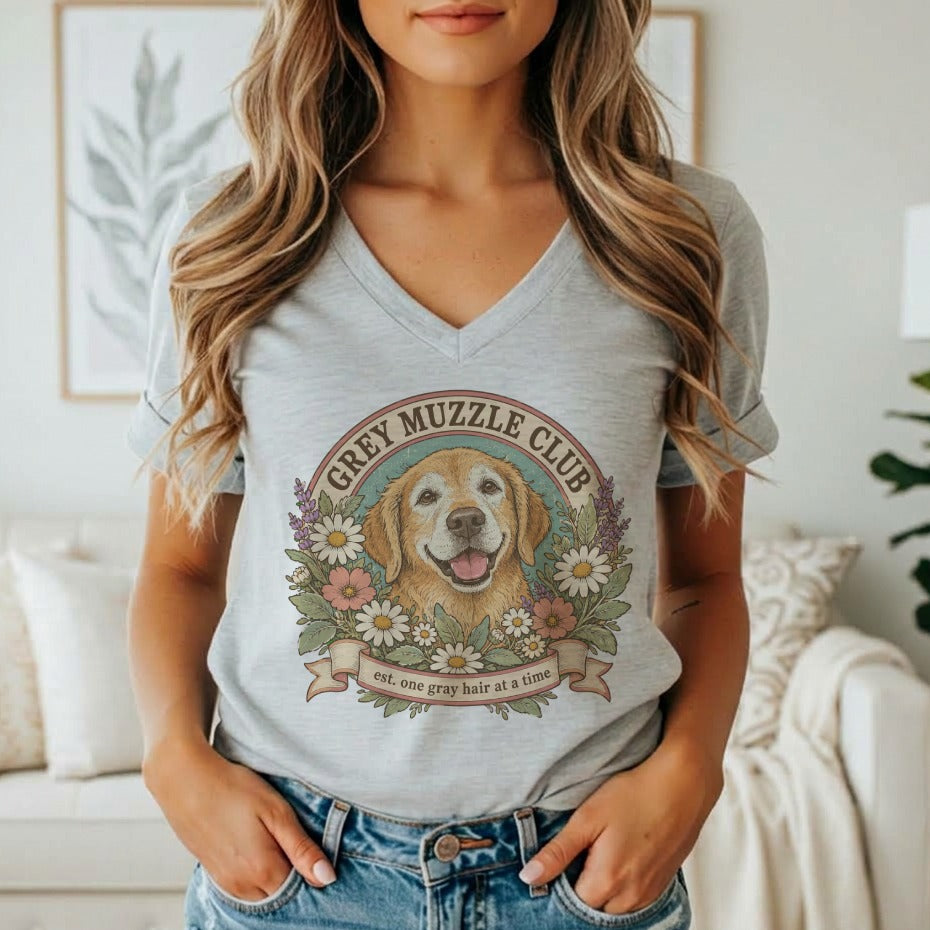 A person wearing a grey v-neck t-shirt featuring a vintage Golden Retriever graphic and the text Grey Muzzle Club.
