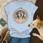 A light blue t-shirt with an embroidered design featuring a dog, flowers, and the text "Silver & Sweet."
