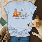Labrador puppies and adult dog sitting around a campfire illustration on a light blue t-shirt.