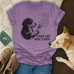 Purple t-shirt with a black and white dog blowing dandelion seeds that form paw prints, text reads "paws and make a wish".