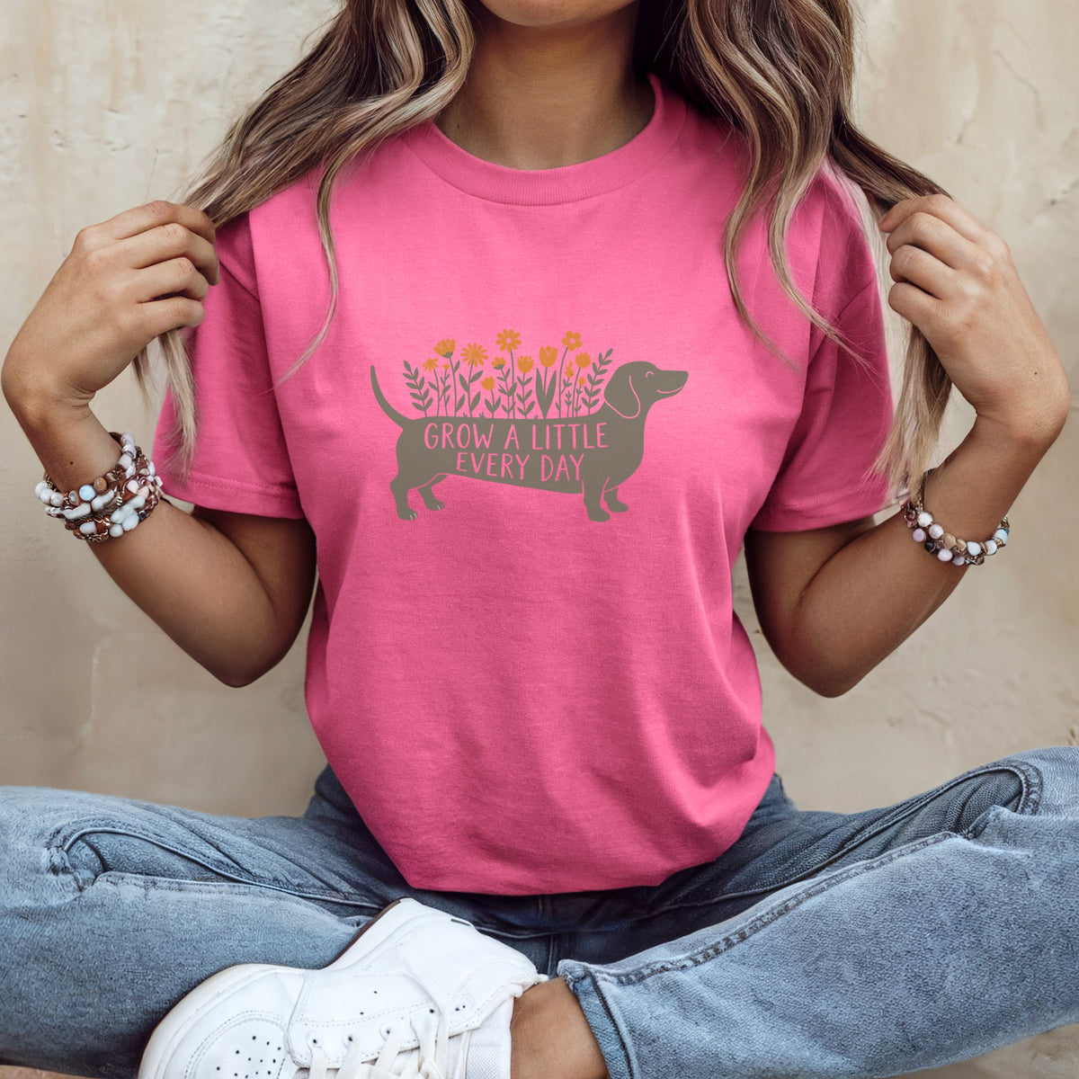 A person wearing a pink t-shirt with a dachshund graphic and text that reads GROW A LITTLE EVERY DAY.