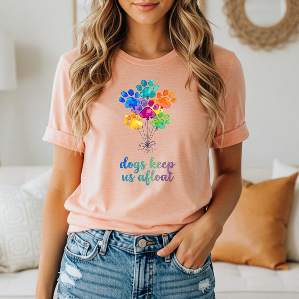 Peach t-shirt with colorful paw print balloons and text: "dogs keep us afloat".