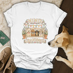 A white V-neck t-shirt featuring a graphic of four dogs on a bench with text reading MIMI'S GRANDDOGS.