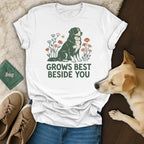 A white t-shirt featuring a graphic of a dog and flowers with the text "GROWS BEST BESIDE YOU."