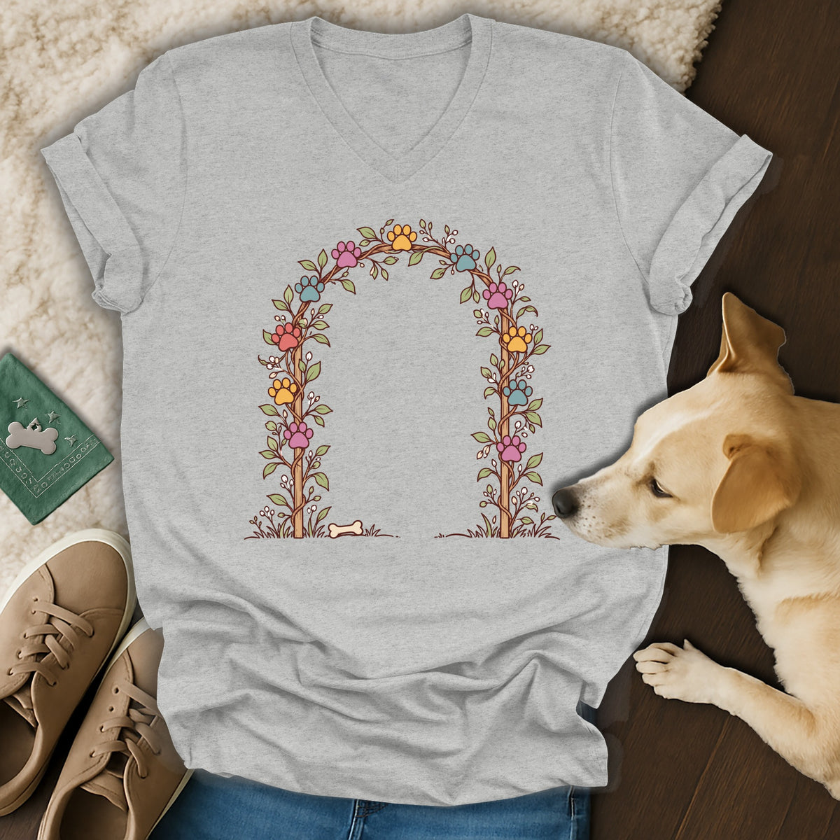 Gray v-neck t-shirt featuring a colorful floral arch graphic with paw prints, laid flat alongside sneakers and a small dog.