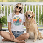 Woman in a t-shirt with a dog graphic and text, posing with a golden retriever.