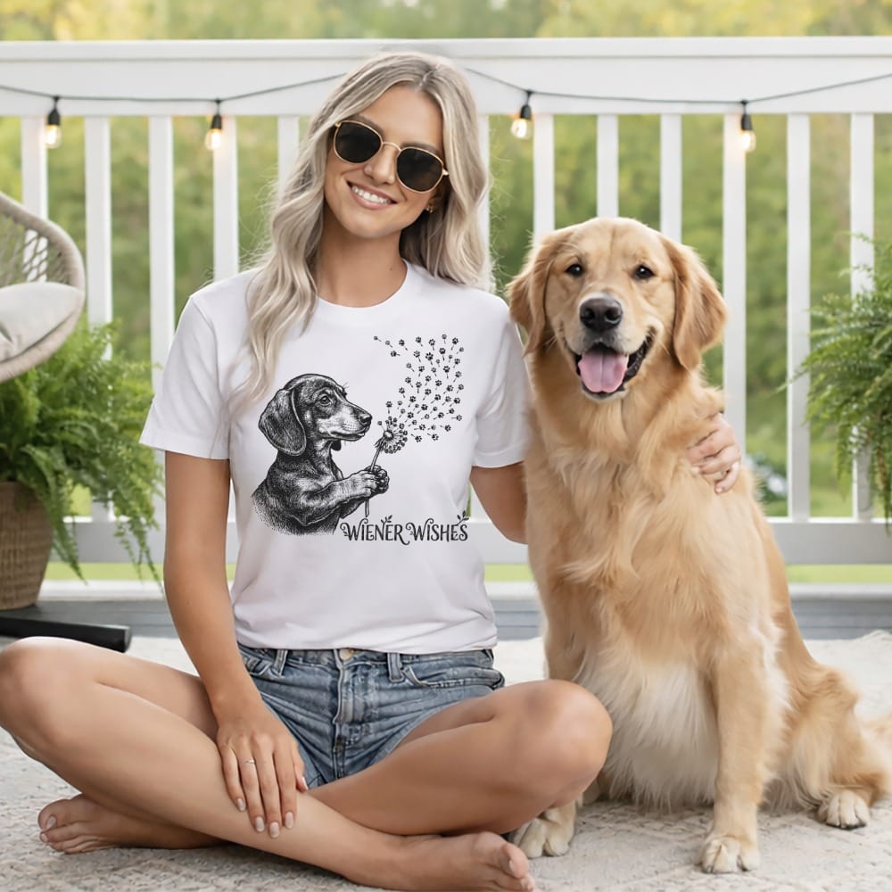 Woman in white t-shirt with dachshund and dandelion design sits with golden retriever.
