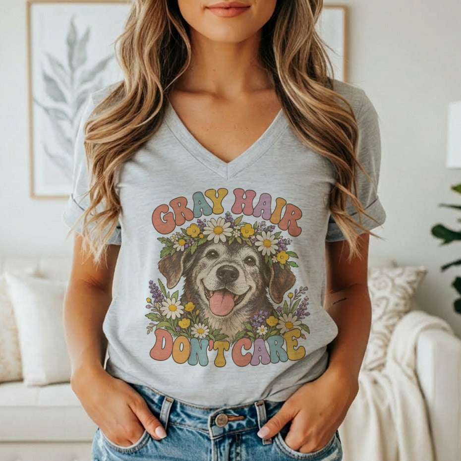 A woman wearing a gray V-neck t-shirt featuring a graphic of a dog wearing a flower crown and the text gray hair don't care.