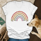 White V-neck t-shirt featuring a colorful rainbow made of paw prints, laid out with shoes and a dog.