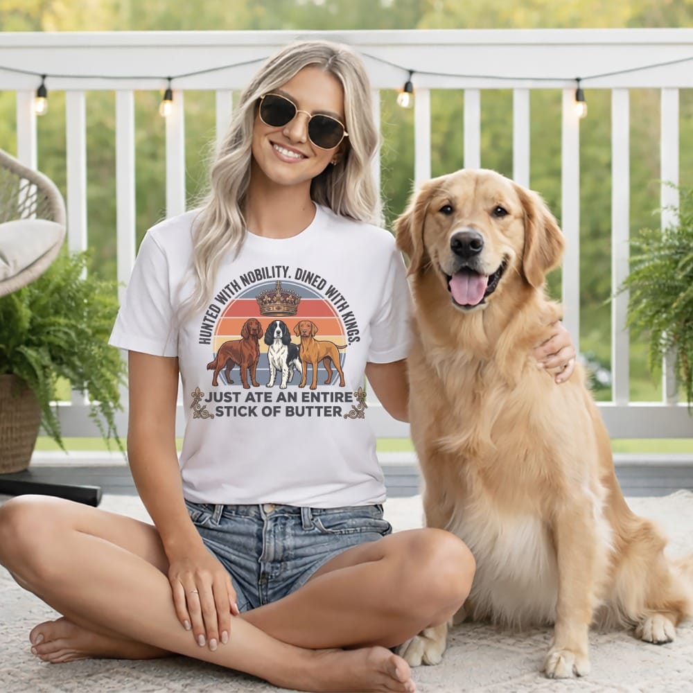 Woman sitting with a golden retriever wearing a shirt that says "HUNTED WITH MOBILITY, DINED WITH KINGS JUST ATE AN ENTIRE STICK OF BUTTER".