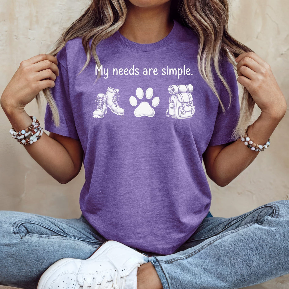Purple t-shirt with "My needs are simple." and hiking icons: boots, paw print, backpack.
