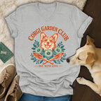 A gray V-neck t-shirt featuring a vintage Corgi Garden Club graphic with crossed trowels and flowers.