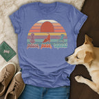 T-shirt with retro sunset design and text "paws, pose, repeat" featuring dog silhouettes.