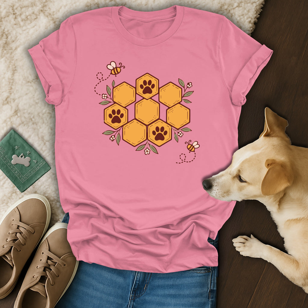 Pink t-shirt with a honeycomb paw print design, surrounded by bees and flowers, laid flat with shoes and a dog.