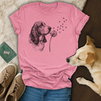 Basset Hound blowing dandelion seeds, pink t-shirt, dog, jeans, sneakers, wooden floor.