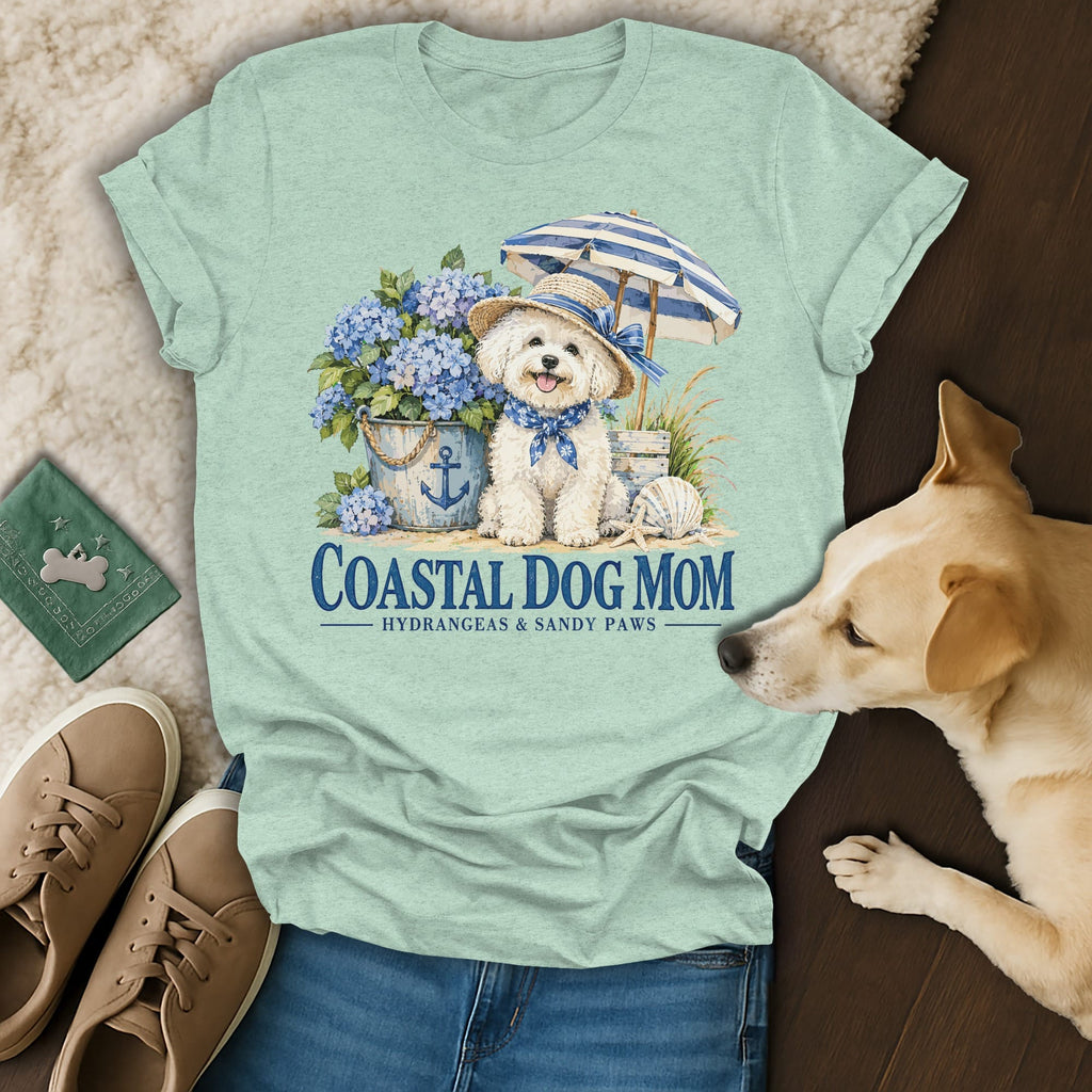 Mint green t-shirt with a graphic of a white dog wearing a hat, umbrella, and hydrangeas, featuring the text Coastal Dog Mom.