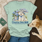 Mint green t-shirt with a graphic of a white dog wearing a hat, umbrella, and hydrangeas, featuring the text Coastal Dog Mom.