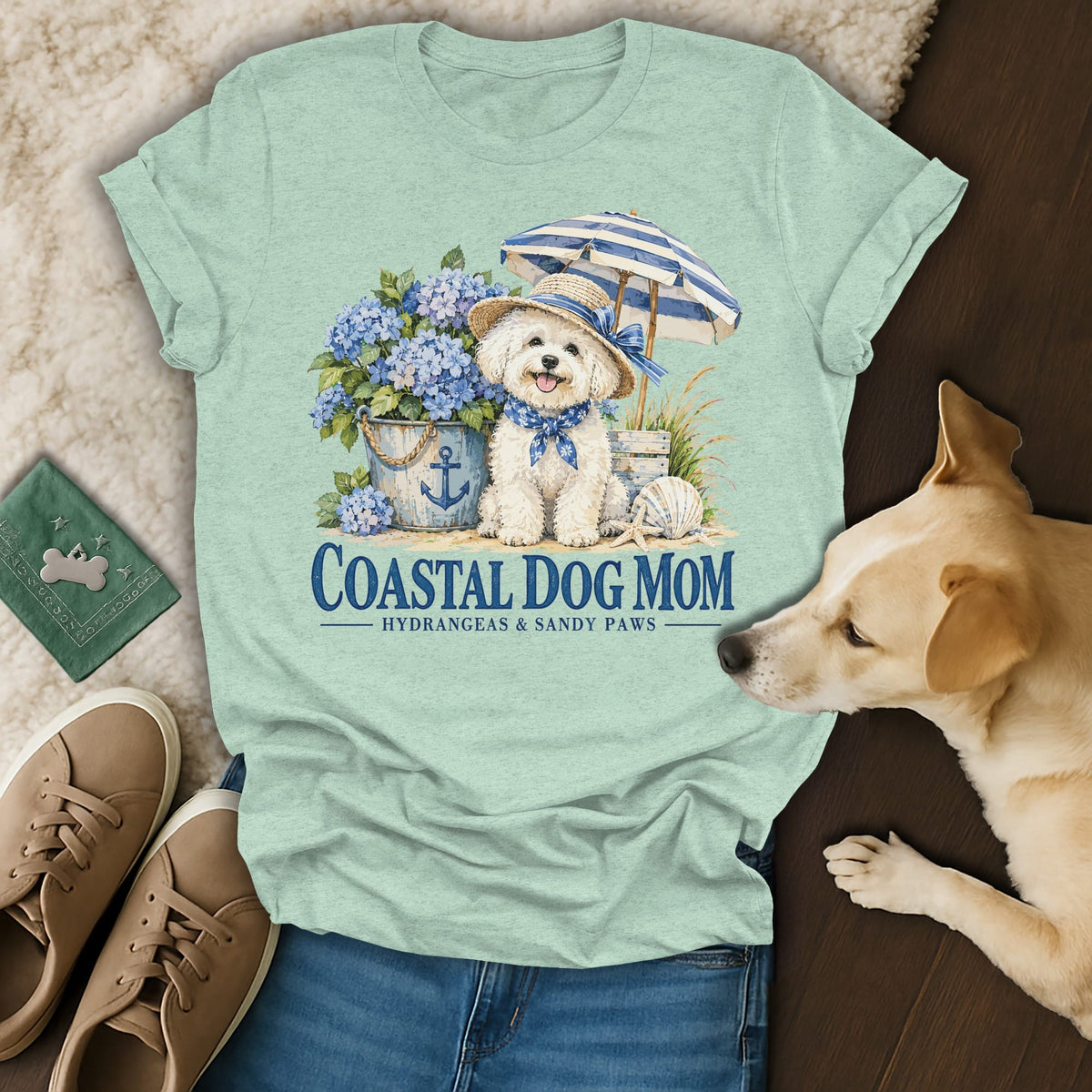 Mint green t-shirt with a graphic of a white dog wearing a hat, umbrella, and hydrangeas, featuring the text Coastal Dog Mom.