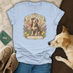 Light blue t-shirt featuring a vintage botanical graphic of a senior dog, surrounded by jeans, sneakers, and a live dog.