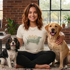 Smiling woman wearing a graphic t-shirt sitting on the floor flanked by two dogs.