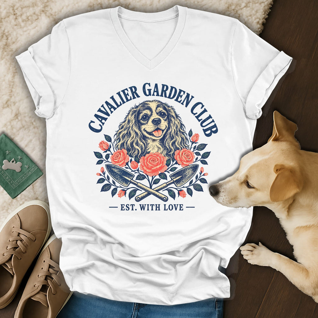 A white V-neck t-shirt featuring a Cavalier King Charles Spaniel graphic with flowers and gardening tools.