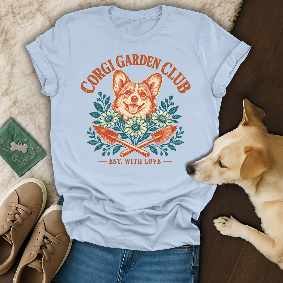 A light blue t-shirt with a vintage Corgi Garden Club graphic featuring a dog, flowers, and garden trowels.