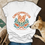 White v-neck t-shirt featuring a Corgi Garden Club graphic with flowers, trowels, and a dog's head.