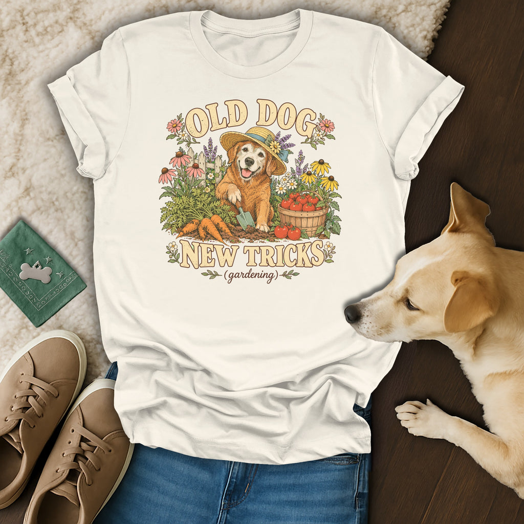 A cream-colored t-shirt with a vintage graphic of a gardening dog surrounded by flowers, carrots, and tomatoes.