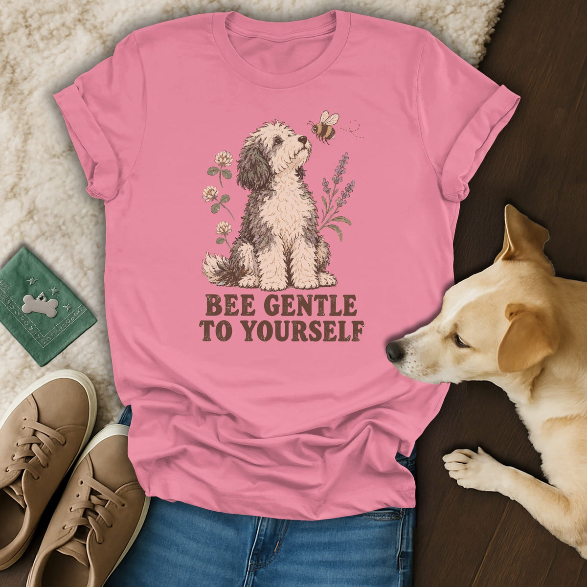 A pink t-shirt with a graphic of a dog, flowers, bee, and the text "BEE GENTLE TO YOURSELF."