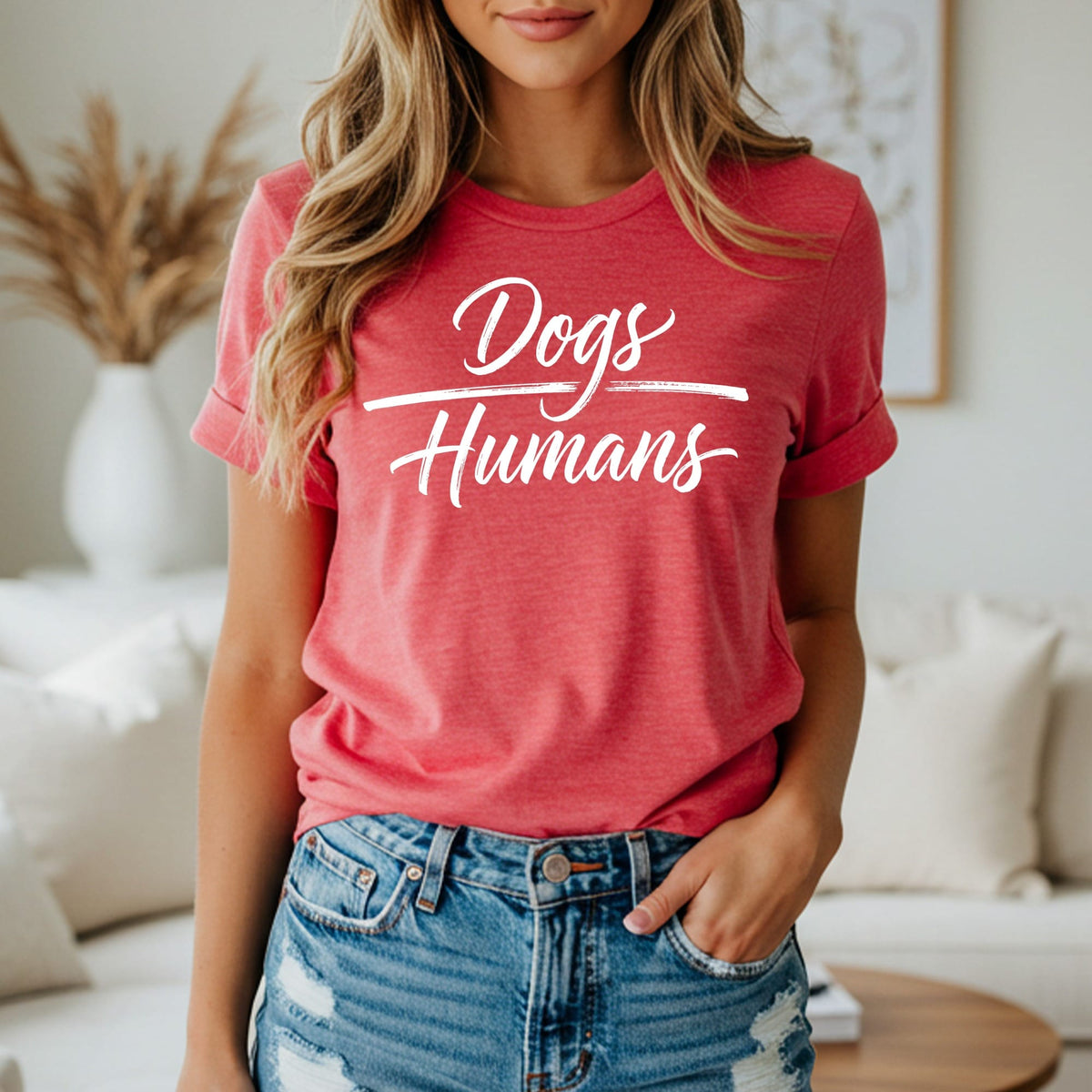 Coral t-shirt with white text "Dogs Humans" against a blurred background.