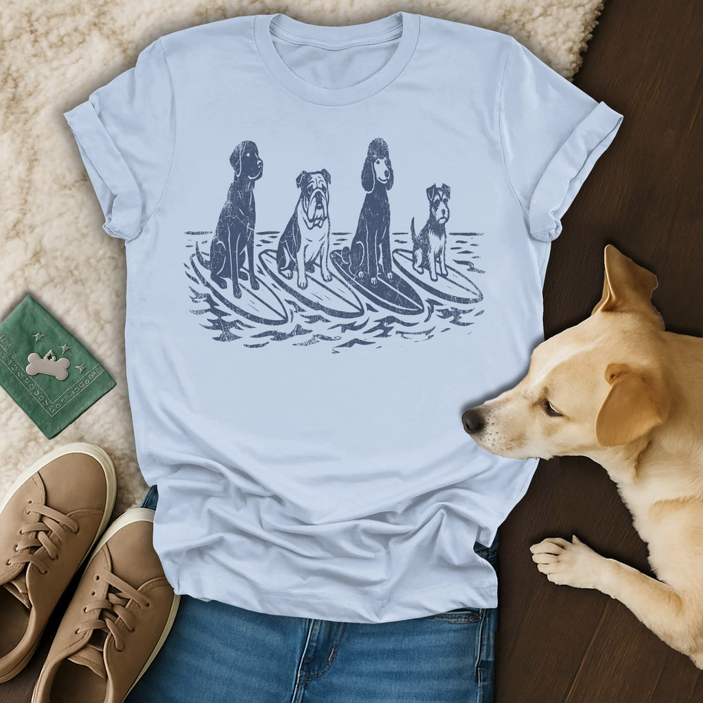 Four dogs of different breeds surf on waves in a distressed graphic on a light blue t-shirt.