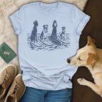 Four dogs of different breeds surf on waves in a distressed graphic on a light blue t-shirt.