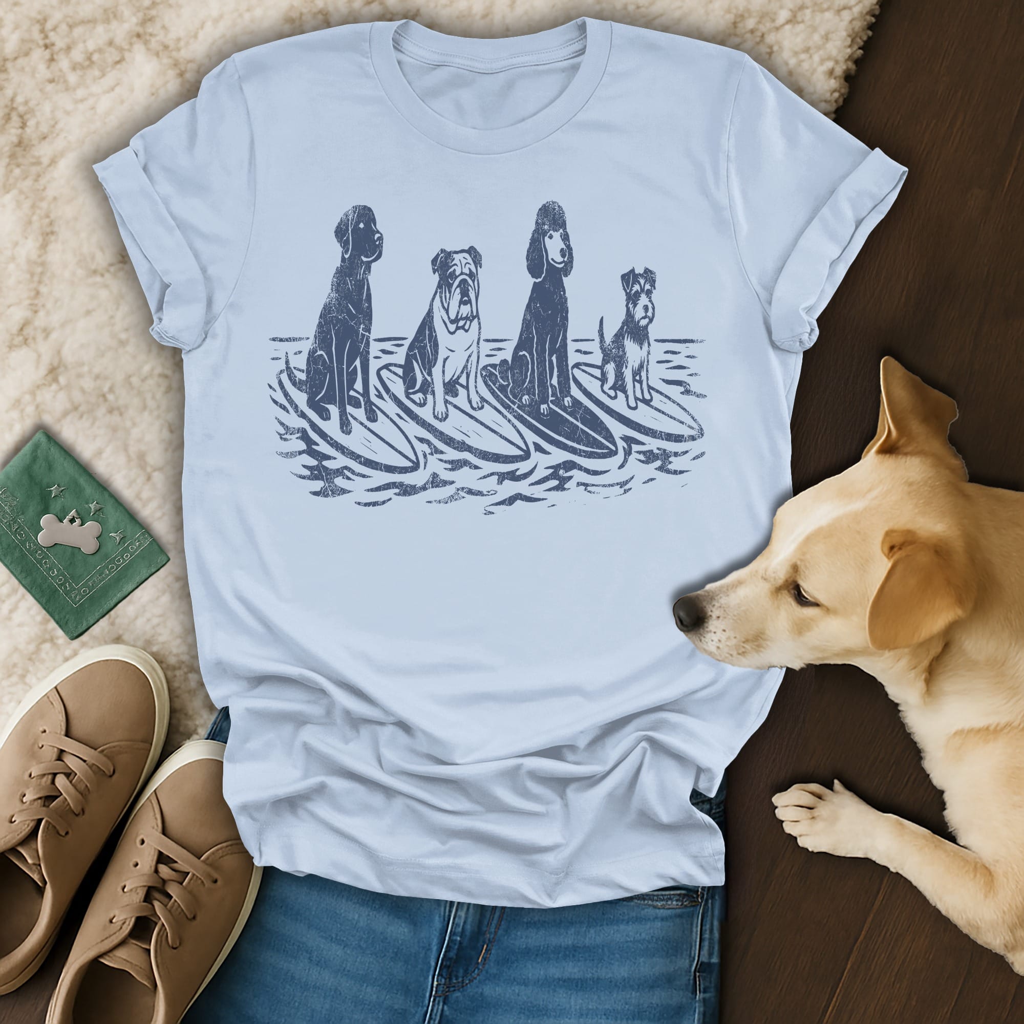 Four dogs of different breeds surf on waves in a distressed graphic on a light blue t-shirt.