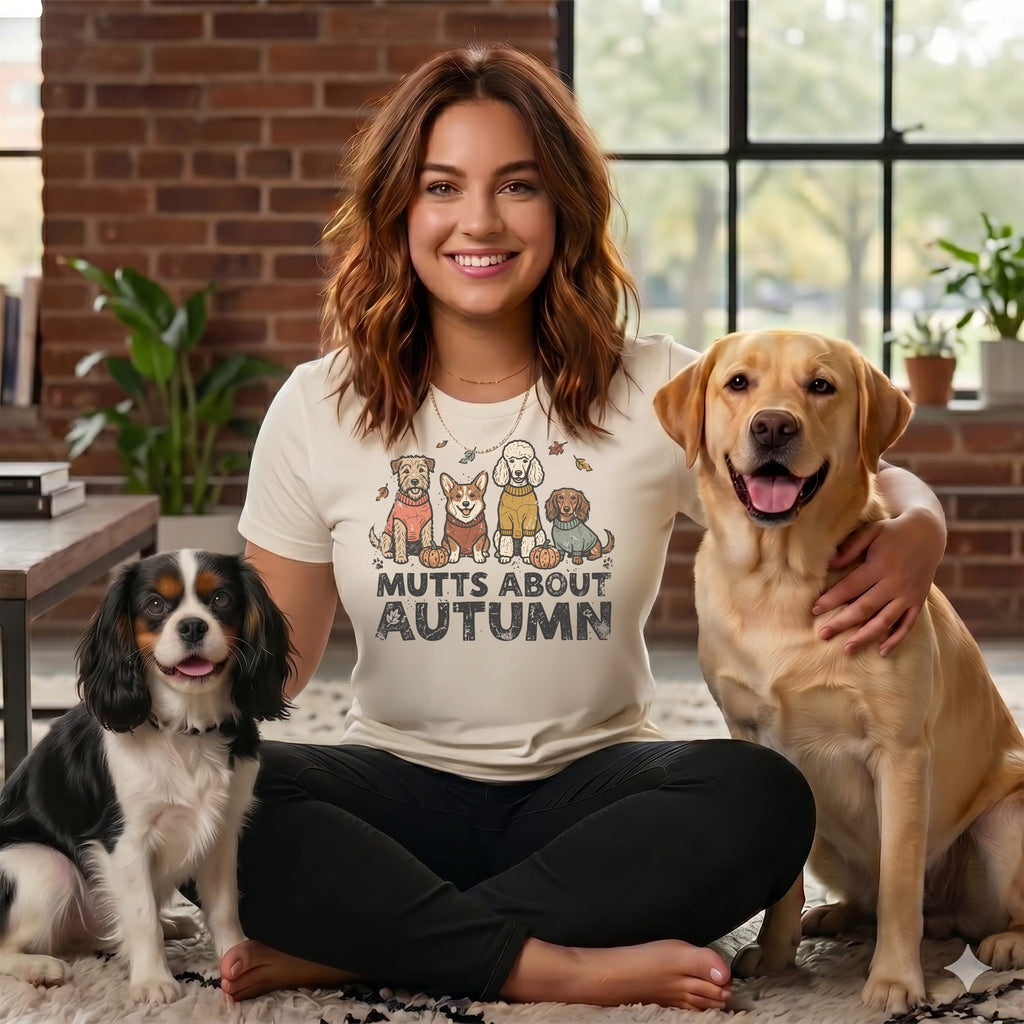 Woman in "Mutts About Autumn" shirt with three dogs: a black and white spaniel, a Labrador, and a shih tzu.