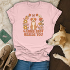 A pink t-shirt with a cartoon dog and floral graphic that reads GROWS BEST BESIDE YOU.