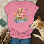 Pink t-shirt with watercolor dog, flowers, watering can, and butterfly graphic.