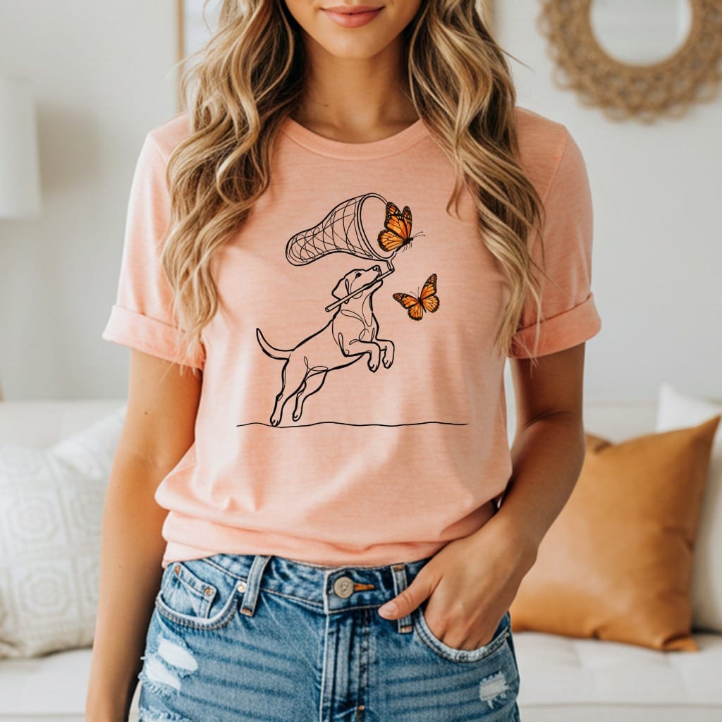 Line drawing of a dog catching butterflies with a net on a peach t-shirt.