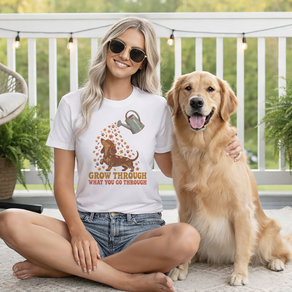 A smiling blonde woman wearing a white graphic t-shirt and sunglasses sits on a deck next to a golden retriever.
