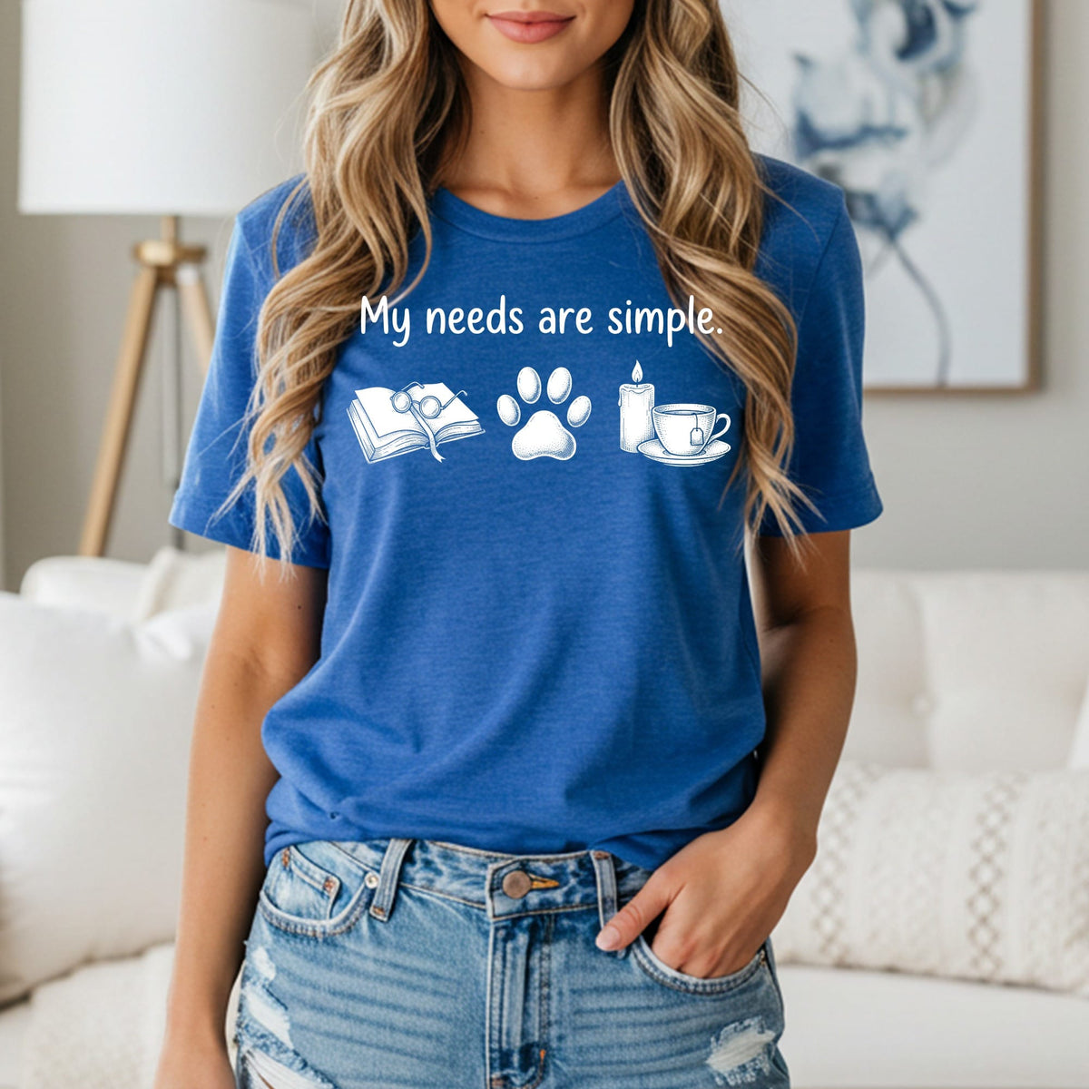 Blue t-shirt with "My needs are simple." text, book, paw print, candle and tea cup icons.