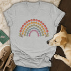 A gray V-neck t-shirt featuring a colorful rainbow made of paw prints, laid flat with shoes and a dog.