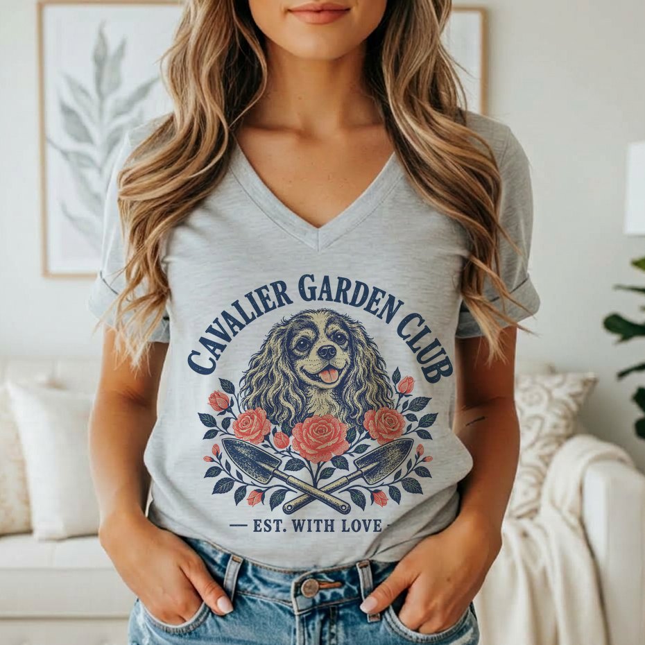 A person wearing a grey V-neck t-shirt featuring a Cavalier King Charles Spaniel graphic with roses, garden trowels, and text.