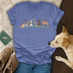 T-shirt with cartoon dogs wearing leis and flowers, on a flat lay with jeans and sneakers.