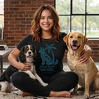 Woman sitting with King Charles Spaniel and yellow Labrador, wearing t-shirt with dog and palm tree graphic.