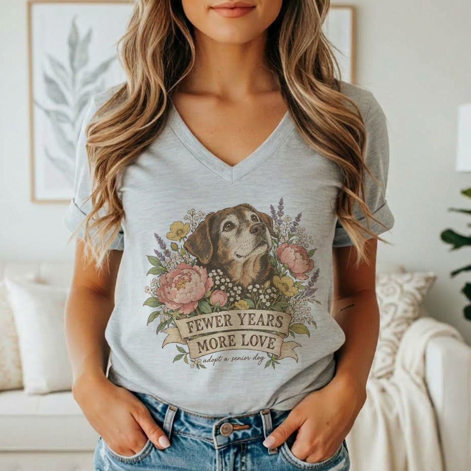 A woman wears a gray V-neck t-shirt featuring a vintage floral dog illustration and text reading FEWER YEARS MORE LOVE.