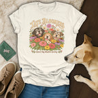Off-white t-shirt with a vintage graphic of three smiling dogs surrounded by colorful flowers and the text Late Bloomers.