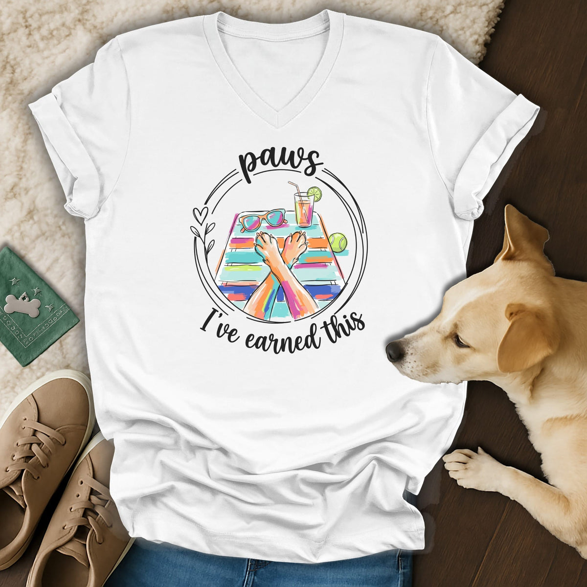 White t-shirt with colorful graphic of dog paws relaxing on a beach towel.