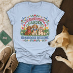 Light blue t-shirt featuring a cross-stitch design of three dogs and the text Grandma's Garden Granddogs Welcome.