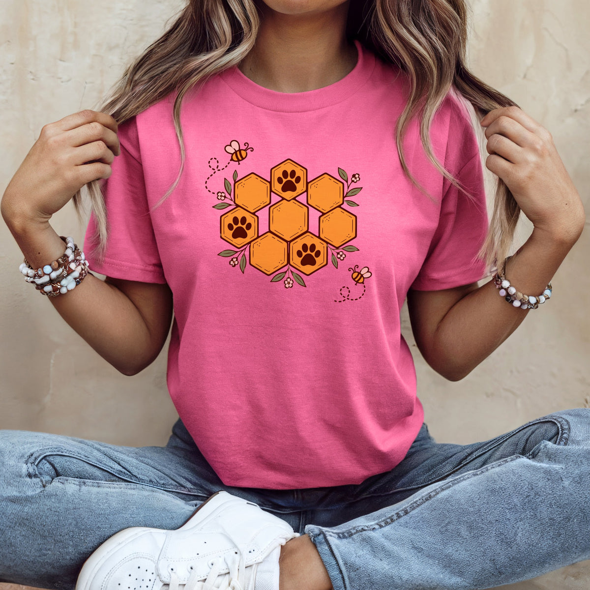 A woman wearing a pink t-shirt with a honeycomb design featuring paw prints and bees.