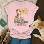 A pink t-shirt featuring an Australian Shepherd graphic and the text "Spread Some Joy," surrounded by shoes, a green wallet, and a dog lying nearby.